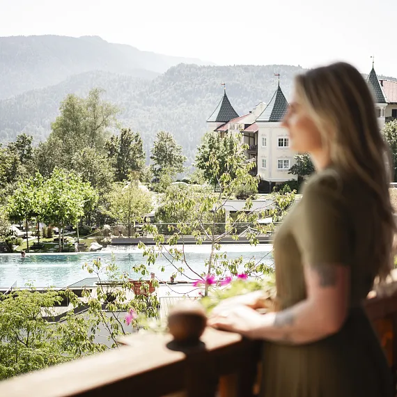 Zwei Personen stehen auf einem Balkon mit Blick auf einen Infinity-Pool, Bäume und Berge in Kitzbühel, Tirol.