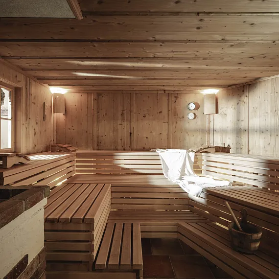 Leere Holzsauna mit Bänken, einem Saunaeimer und Handtüchern auf der linken Bank, warm beleuchtet.