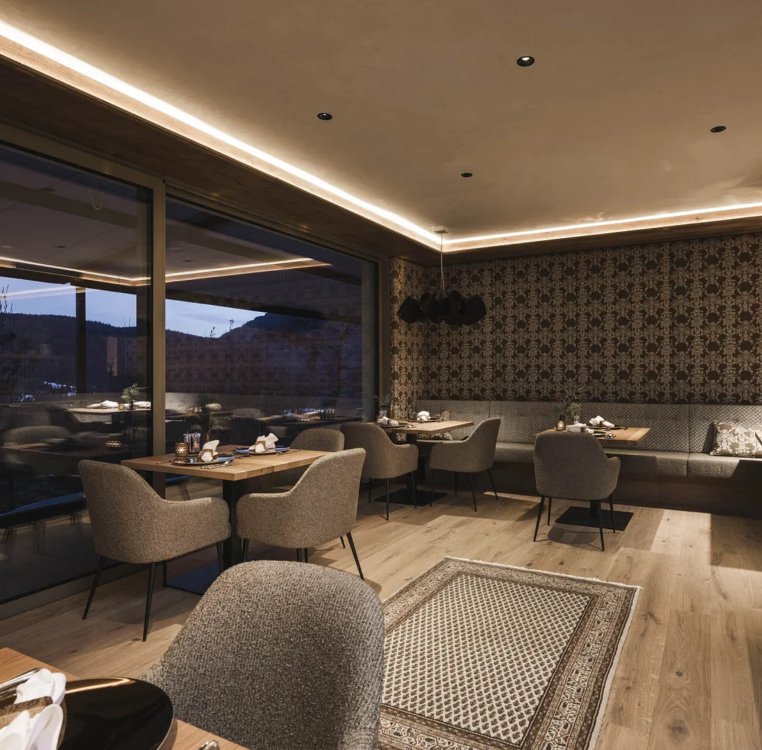 Modernes Restaurantinterieur mit gedeckten Tischen, stilvollen Sesseln und großem Fenster.