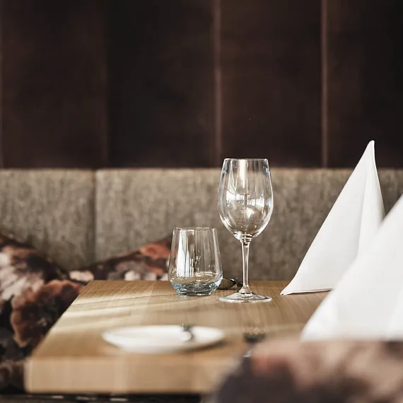 Leere Weingläser und ein Wasserglas auf einem Holztisch in einem eleganten Restaurantambiente.