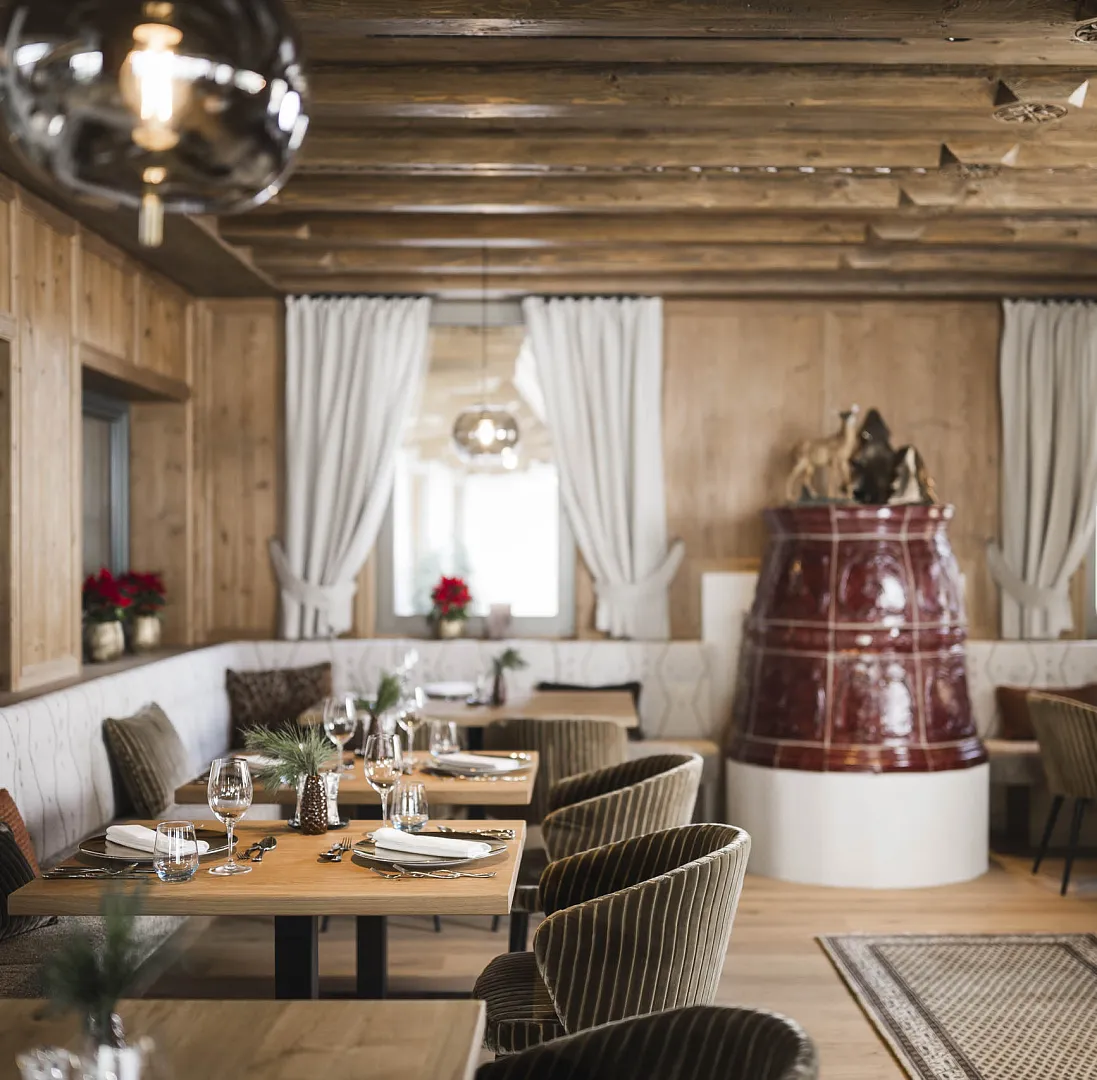 Gemütliches Restaurant in Tirol mit Holzwänden, Tischen aus Holz und einem roten Kachelofen.