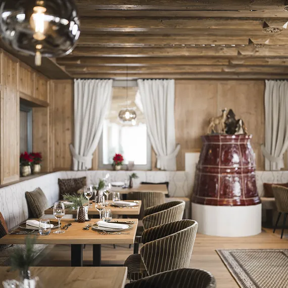 Cozy restaurant with wooden decor, red ceramic stove, and set tables, located in a rustic setting.