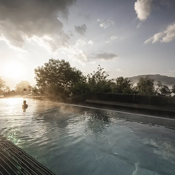 Person schwimmt in einem Infinity-Pool mit Blick auf die Berge bei Sonnenaufgang in Tirol.
