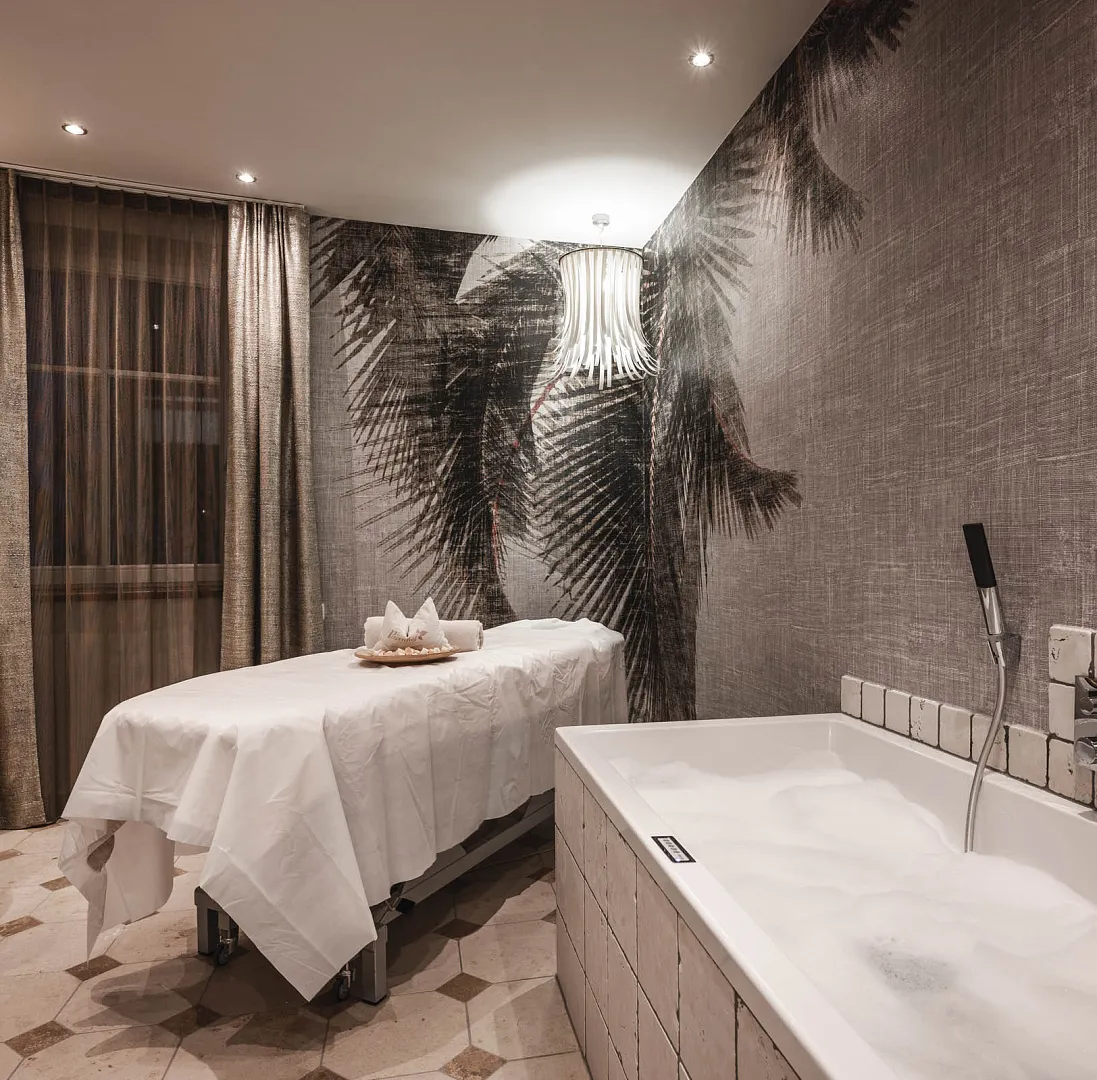 Wellnessraum mit Massageliege, Badewanne und neutraler Dekoration in warmen Tönen.