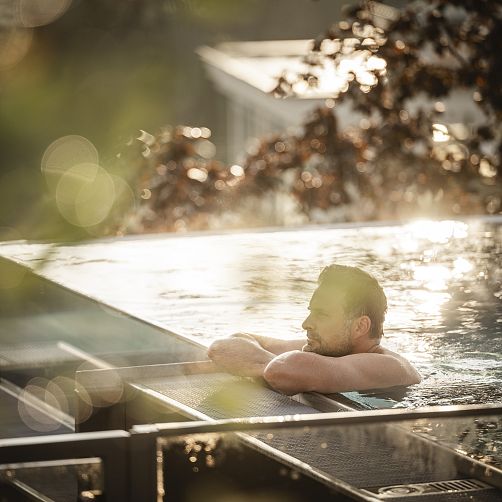 Mann entspannt in einem Infinity-Pool bei Sonnenuntergang.