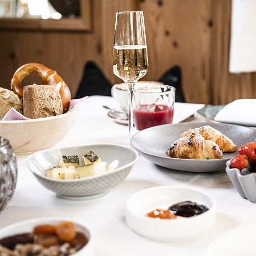Frühstückstisch mit Croissants, Brötchen, Käse und Getränken in einem gemütlichen Setting.