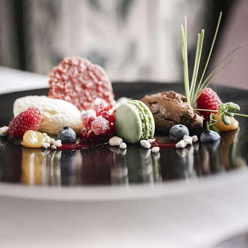 Elegante Dessertplatte mit Macaron, Eiscreme-Kugeln und frischen Beeren auf schwarzem Teller.