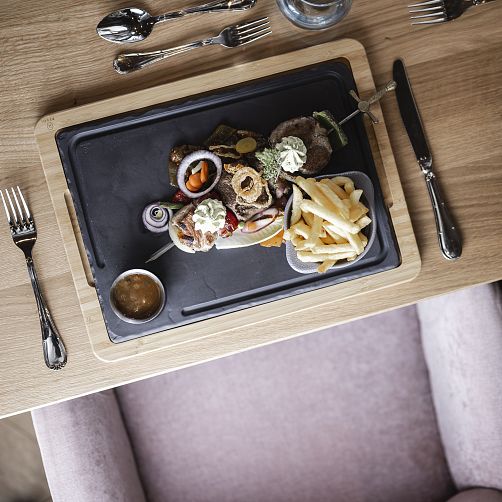 Servierteller mit Fleisch, Gemüse und Pommes auf einem Holztisch.