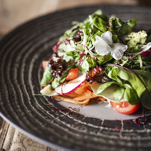 Hochwertiger gemischter Salat mit frischen Zutaten, dekorativ auf einem grauen Teller angerichtet.