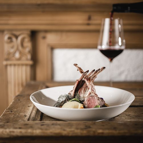 Gehobenes Gericht mit Lammrippen, Gemüsebeilage und ein Glas Rotwein auf einem Holztisch.