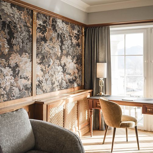Gemütlicher Arbeitsbereich in einem Tiroler Hotelzimmer mit Holzmöbeln und Ausblick auf verschneite Berge.
