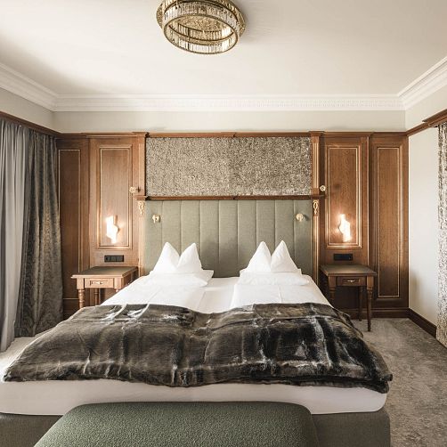 Elegantes Hotelzimmer in Tirol mit Doppelbett, Holzvertäfelung und modernen Leuchten.