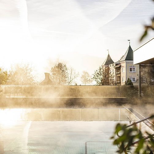 Historisches Gebäude mit Türmen hinter einem dampfenden Pool in einer Herbstlandschaft.