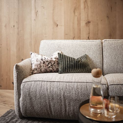 Graues Sofa mit dekorativen Kissen vor einer Holzwand.