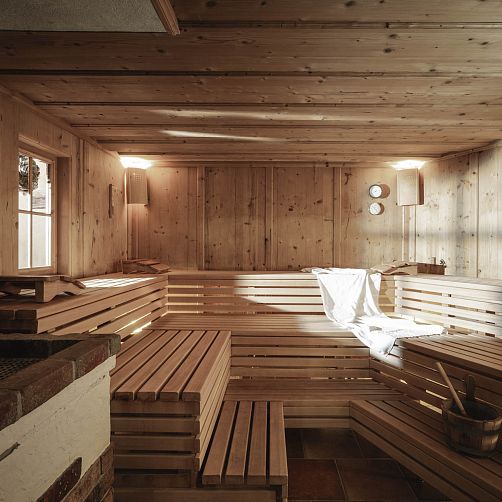 Holzverkleidete Sauna mit Holzbänken und Handtuch, warmes Licht und zwei runde Wandthermometer.