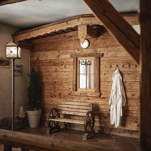 Rustikaler Raum mit Holzwänden, Fenster, Bank und weißen Bademänteln an Haken.