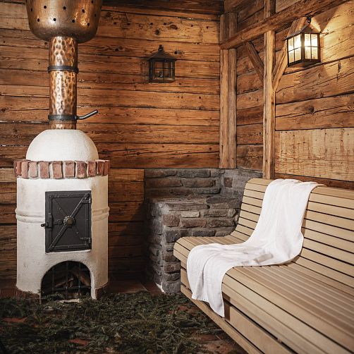 Traditionelle Holzsauna mit Steinofen und Holzbank, beleuchtet von Wandleuchten.