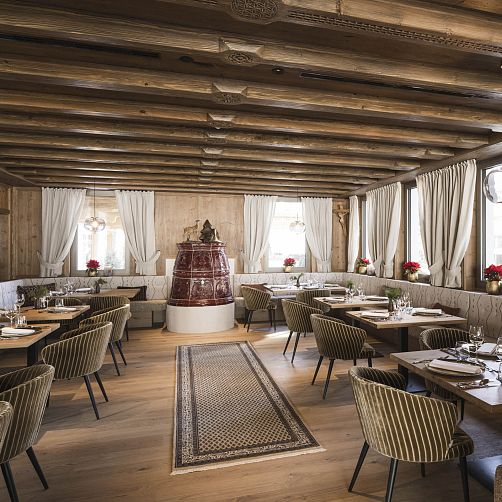 Elegantes Restaurant mit Holzbalkendecke, roten Dekoelementen und gedeckten Tischen, Tiroler Stil.