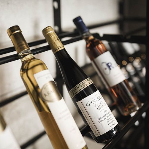 Drei Flaschen Wein auf einem Weinregal, etikettiert und schräg geneigt präsentiert.
