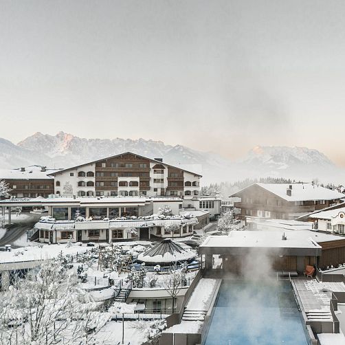 Winterliche Hotelanlage mit schneebedeckten Gebäuden und Bergen im Hintergrund in Kitzbühel, Tirol.