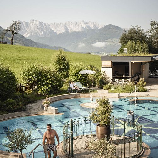 Freiluft-Schwimmbad mit Bergen im Hintergrund, umgeben von grünen Wiesen in Tirol.