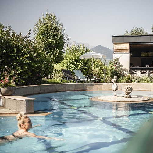 Gartenpool mit Liegestühlen und Sonnenschirm, umgeben von Bäumen, in einer modernen Anlage in Kitzbühel.