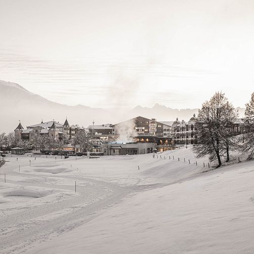 Verschneiter Hang mit Gebäuden im Hintergrund, vermutlich in Kitzbühel, Tirol.