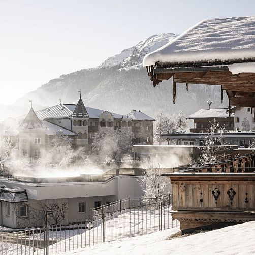 Verschneite Gebäude und Berge in Kitzbühel, Tirol bei klarem Winterwetter, mit Dampf über einem Hausdach.