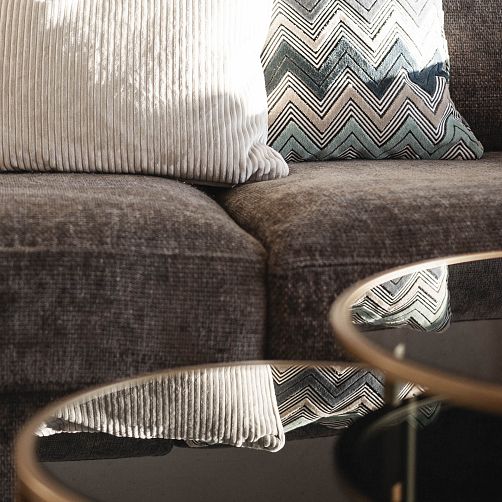 Graues Sofa mit strukturierten Kissen, im Vordergrund runde Glastische.
