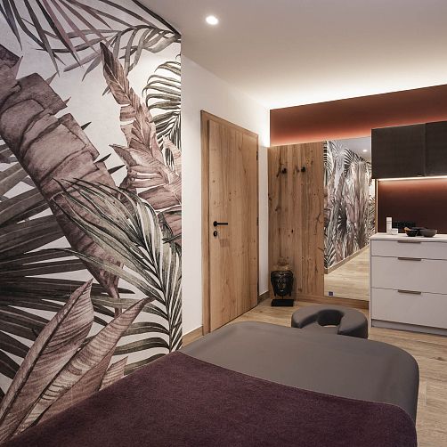 Modernes Spa-Interieur mit Massageliege, Holzakzenten und großem Blattmotiv an der Wand.