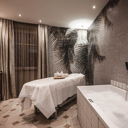 Wellnessraum mit Massageliege, Badewanne und neutraler Dekoration in warmen Tönen.