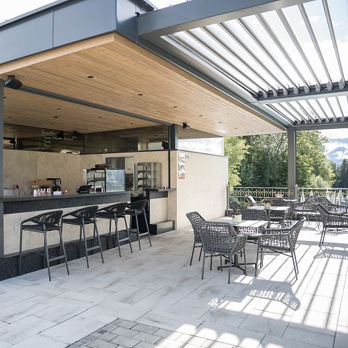 Leere Außenterrasse eines Cafés in den Bergen mit modernen Sitzmöbeln und Holzverkleidung.
