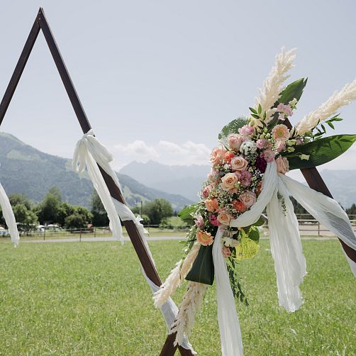 Dreieckiger Holzrahmen mit Blumenarrangement vor Berglandschaft in Tirol.