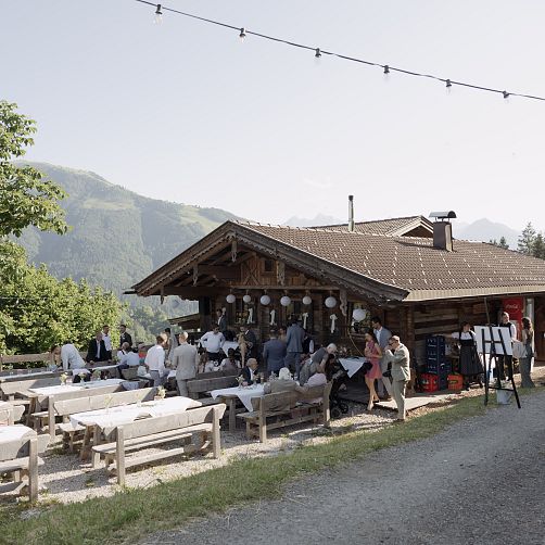 Freiluftveranstaltung an einer Berghütte in Tirol mit Bergen im Hintergrund und Menschen beim Essen.
