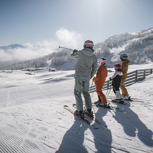 Three skiers stand on a snowy slope in Kitzbühel, observing the mountain view.