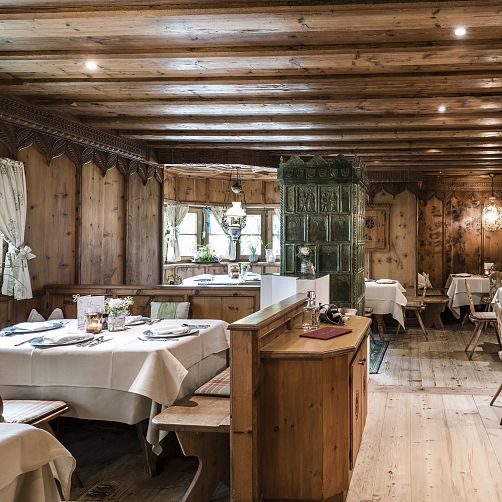 Gemütliches Restaurant im Tiroler Stil mit Holzwänden und einem grünen Kachelofen.