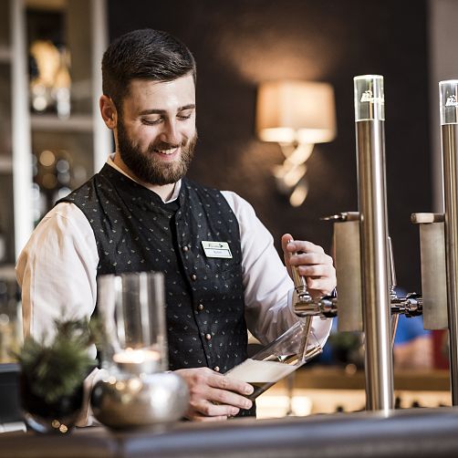 Bärtiger Barkeeper in Kitzbühel schenkt Getränk aus Zapfanlage in einem stilvollen Ambiente ein.