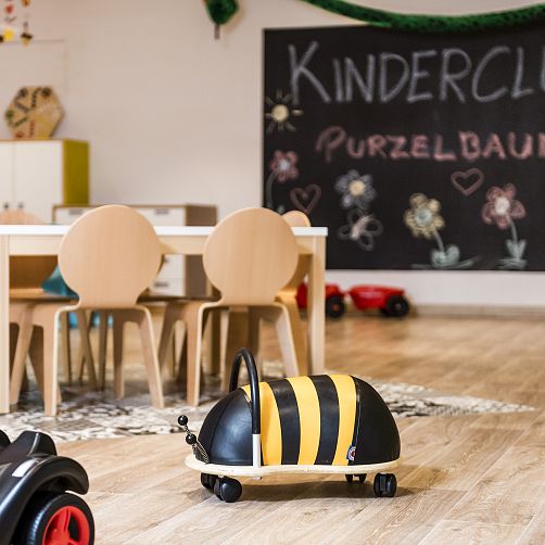 Spielzimmer mit Tisch, Stühlen, Wandtafel und Spielzeugbiene auf dem Boden.