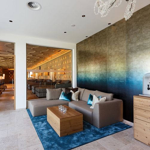 Modernes Wohnzimmer mit grauem Sofa, blauen Kissen und Holztisch, an einer Wand mit Farbverlauf.