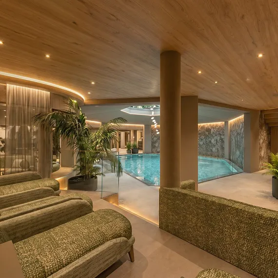 Luxuriöser Innenpoolbereich mit Liegestühlen, Pflanzen und Holzdecke in moderner Spa-Umgebung.