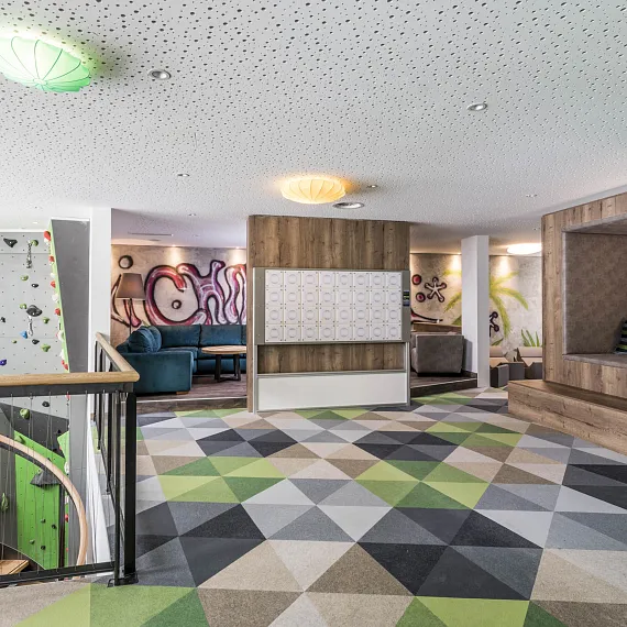 Modern gestalteter Innenraum mit Kletterwand, Sitzalkoven und geometrischem Teppichmuster.