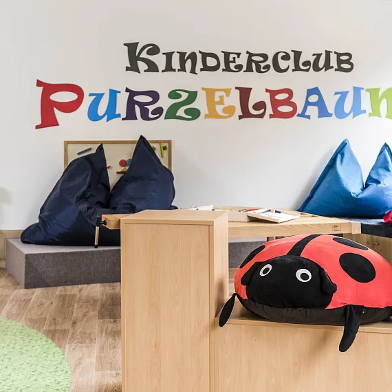 Spielbereich in einem Kinderclub mit bunten Kissen, Bänken und einem Wandbild 'Kinderclub Purzelbaum'.