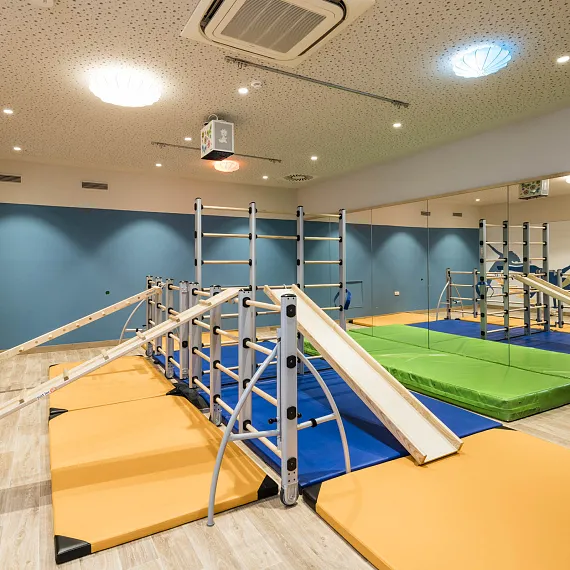 Innenansicht eines modernen Fitnessraums mit Klettergerüsten und Matten auf Holzfußboden.