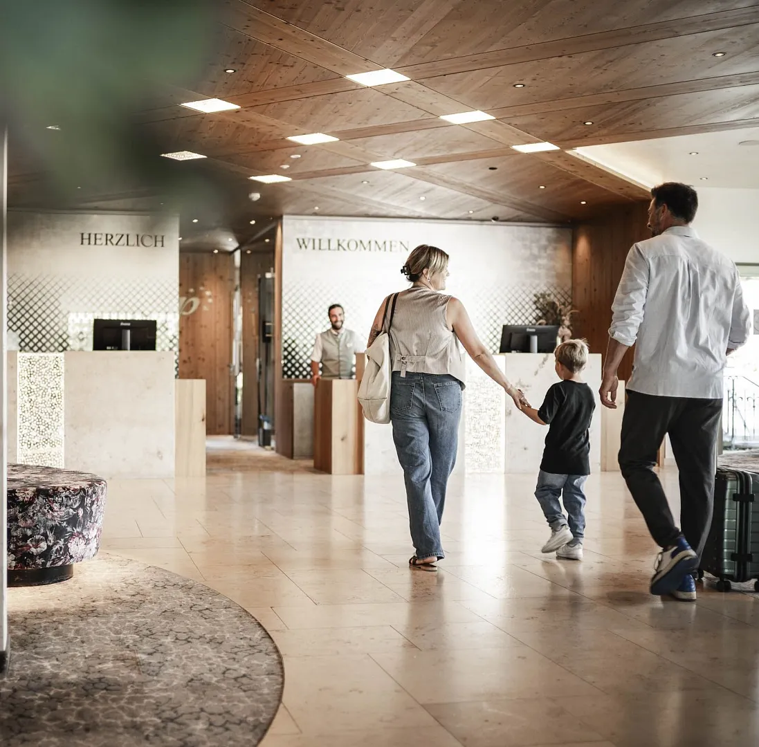 Familie betritt modern gestaltetes Empfangsbereich eines Hotels, dekoriert mit Holz und geometrischen Elementen.